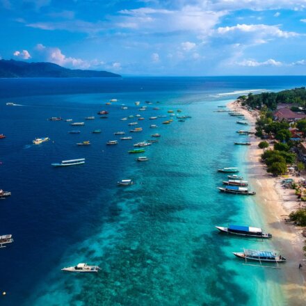 Luftaufnahme der Küste von Lombok mit türkisblauem Meer, vielen Booten und Strand mit Gebäuden und Palmen bei sonnigem Wetter