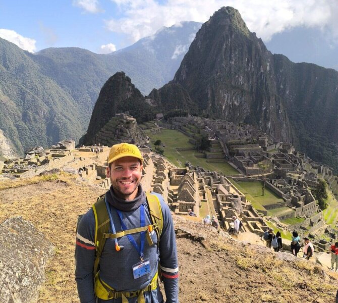Reisender steht lächelnd vor der Ruinenstadt Machu Picchu in den Anden von Peru