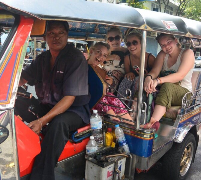 Gruppe von Menschen sitzt in einem bunten Tuk-Tuk mit Fahrer auf einer belebten Straße bei Tag in Bangkok