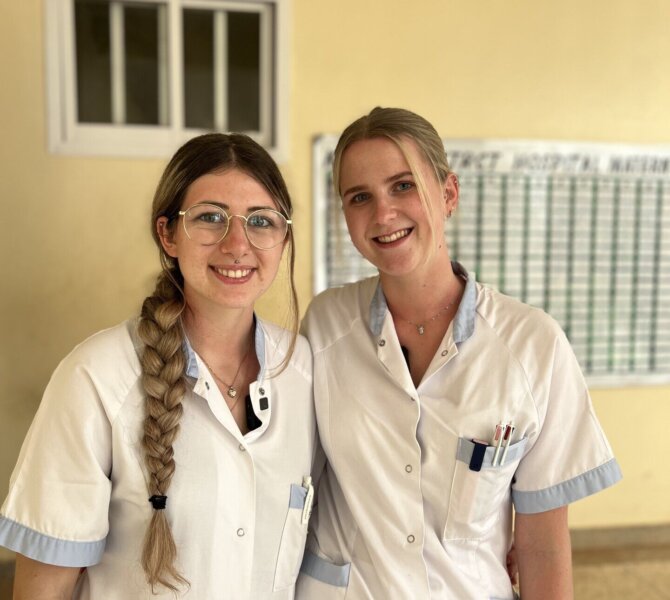 Zwei Frauen in weißer Arbeitskleidung stehen lächelnd in einem Krankenhausflur in Sansibar bei der Freiwilligenarbeit.