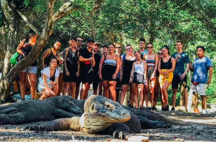 Gruppe junger Reisender beobachtet Komodowarane auf Rinca Island in Indonesien, umgeben von tropischer Natur.