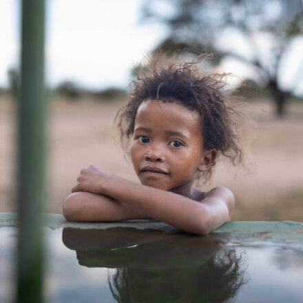 Kind lehnt an Wasserstelle und blickt ruhig in die Kamera in ländlicher Region Afrikas