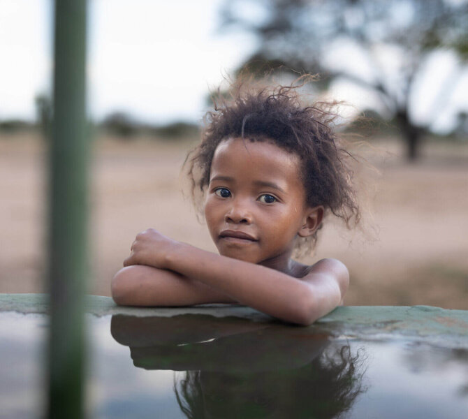 Kind lehnt an Wasserstelle und blickt ruhig in die Kamera in ländlicher Region Afrikas