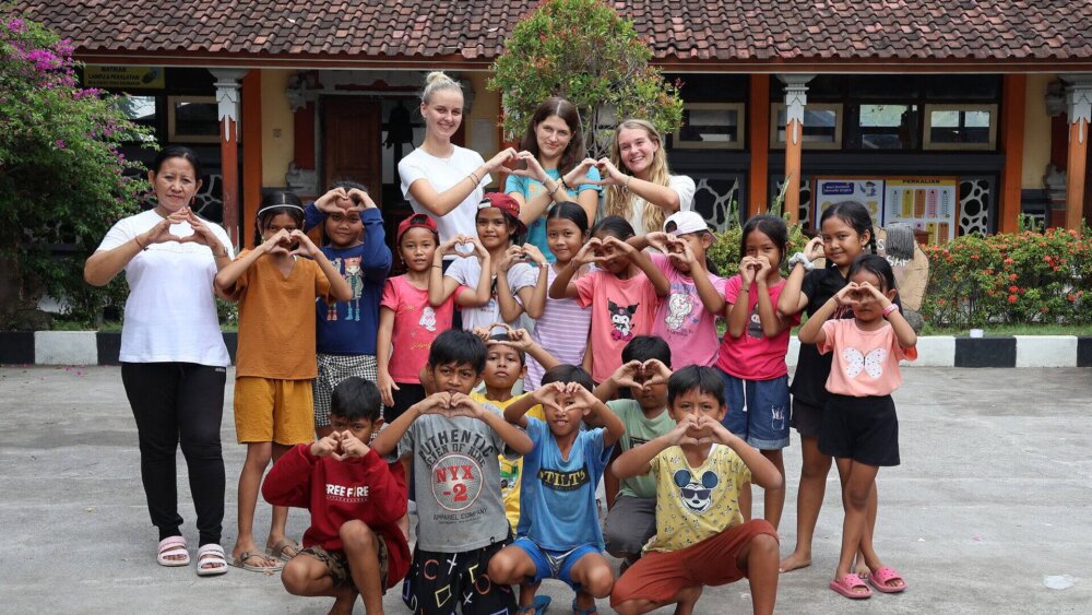 Freiwillige und Kinder formen Herzzeichen im Schulhof während Sozialprojekt mit Wayers auf Bali