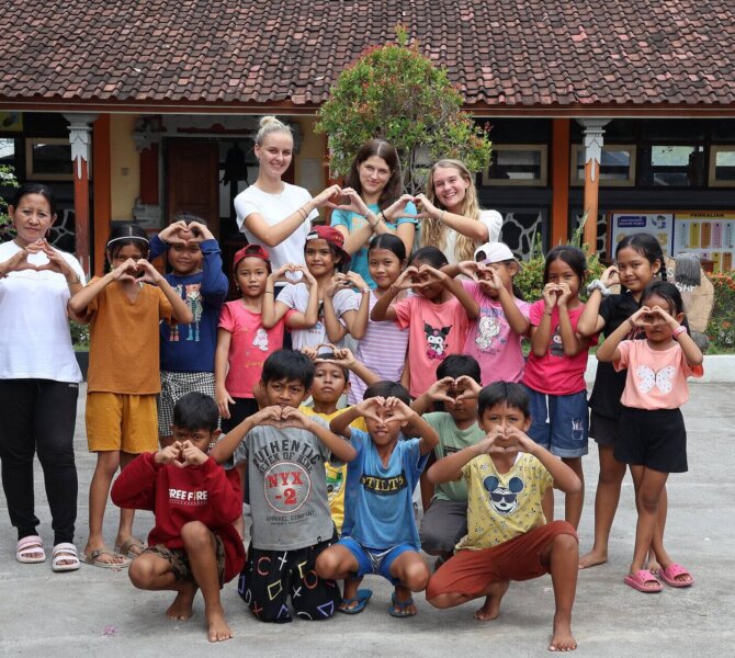 Freiwillige und Kinder formen Herzzeichen im Schulhof während Sozialprojekt mit Wayers auf Bali