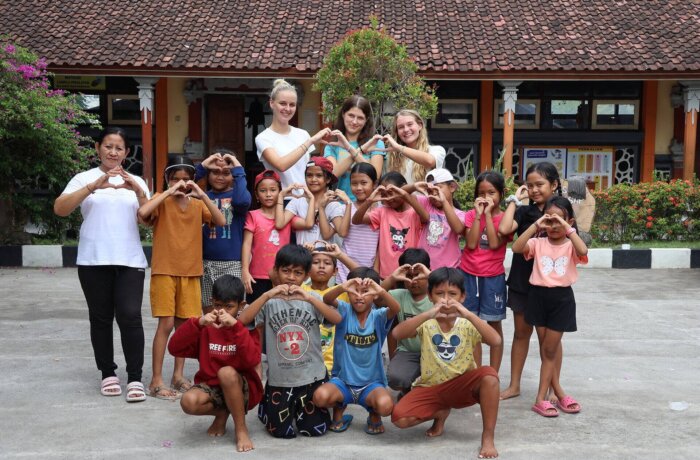 Freiwillige und Kinder formen Herzzeichen im Schulhof während Sozialprojekt mit Wayers auf Bali