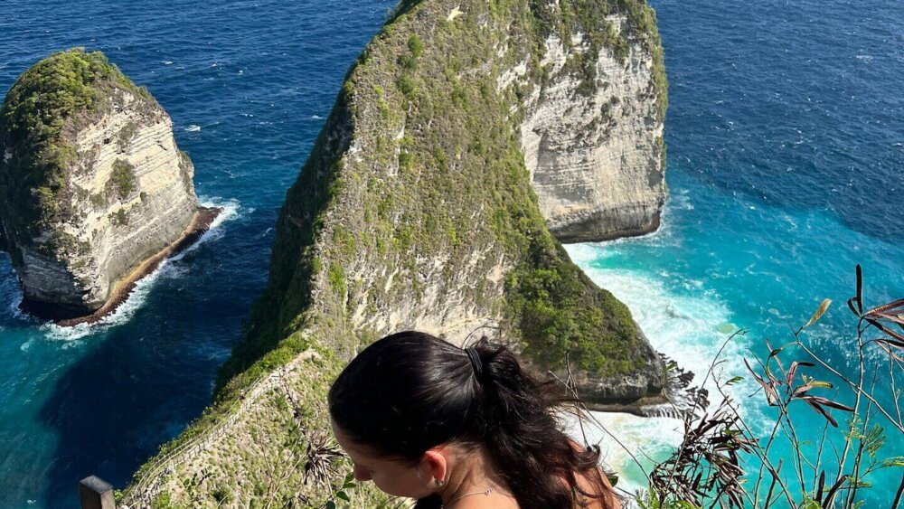 Frau genießt atemberaubenden Ausblick auf Klippen und türkisblaues Meer bei Kelingking Beach auf Nusa Penida, Indonesien.