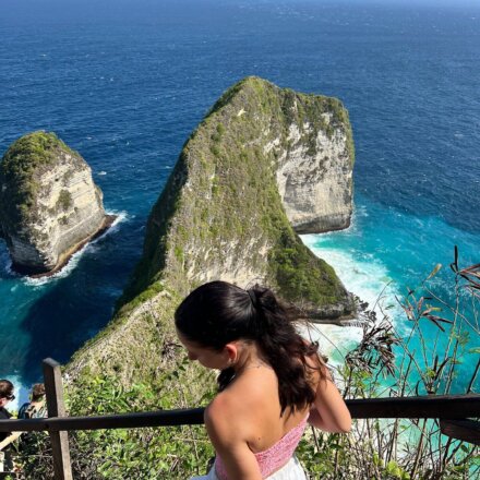 Frau genießt atemberaubenden Ausblick auf Klippen und türkisblaues Meer bei Kelingking Beach auf Nusa Penida, Indonesien.