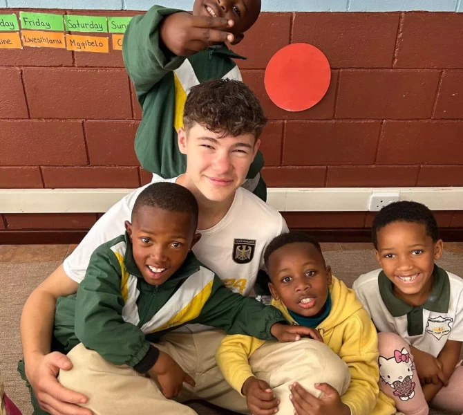 Freiwilliger spielt und lacht mit Schulkindern im Klassenzimmer während Sozialprojekt in Afrika