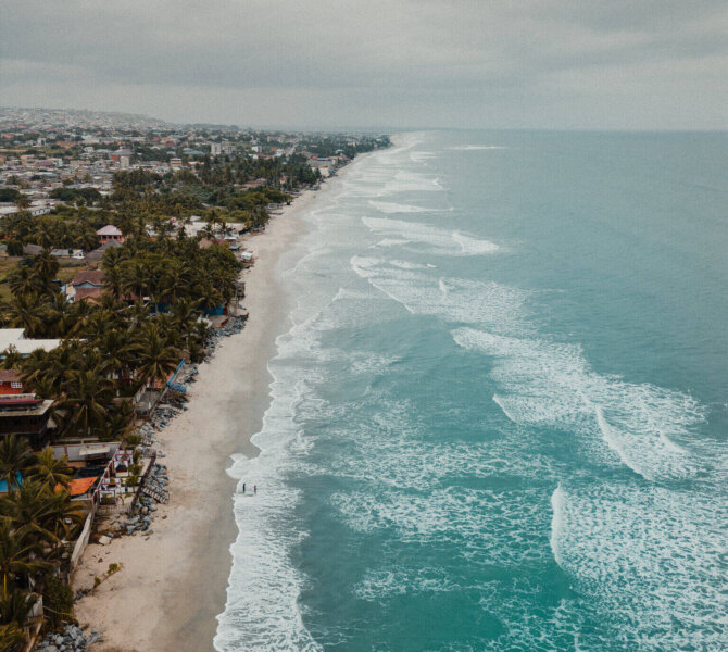 Luftaufnahme einer tropischen Küste mit breitem Sandstrand türkisfarbenem Meer und dichter Bebauung unter bewölktem Himmel