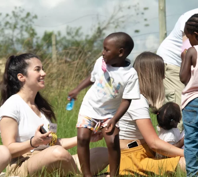 Freiwillige spielen mit Kindern auf einer Wiese bei sonnigem Wetter in Südafrika mit wayers.