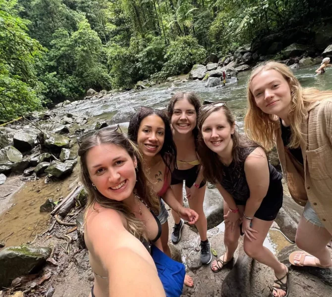 Fünf junge Frauen machen ein Selfie am Flussufer inmitten des tropischen Regenwaldes in Costa Rica.
