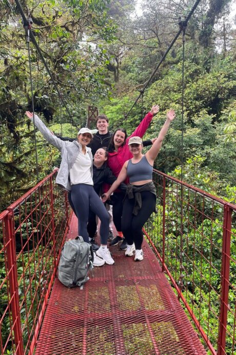 Gruppe fröhlicher Menschen posiert auf einer roten Hängebrücke im Nebelwald von Costa Rica, umgeben von dichtem Grün.
