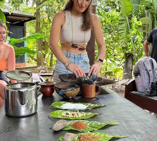 Junge Frau bereitet an einem Tisch mit Zutaten auf Bananenblättern traditionelle Speisen in einem Kochworkshop in Costa Rica zu.