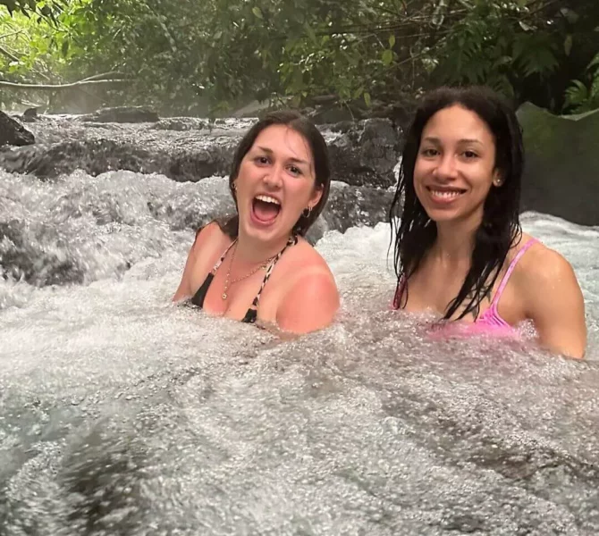 Zwei Frauen baden lachend in einer natürlichen Thermalquelle im tropischen Regenwald von Costa Rica.