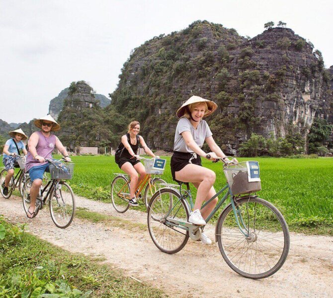 Gruppe von Touristen fährt mit dem Fahrrad durch eine grüne Landschaft in Ninh Binh, umgeben von beeindruckenden Karstfelsen.