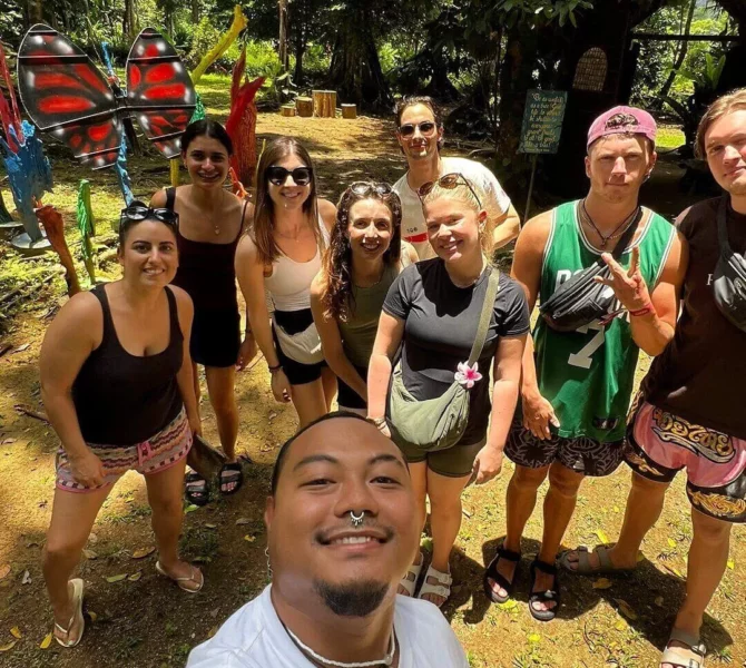 Gruppe junger Menschen macht ein Selfie im tropischen Dschungel auf den Philippinen, umgeben von Kajaks und Bäumen.