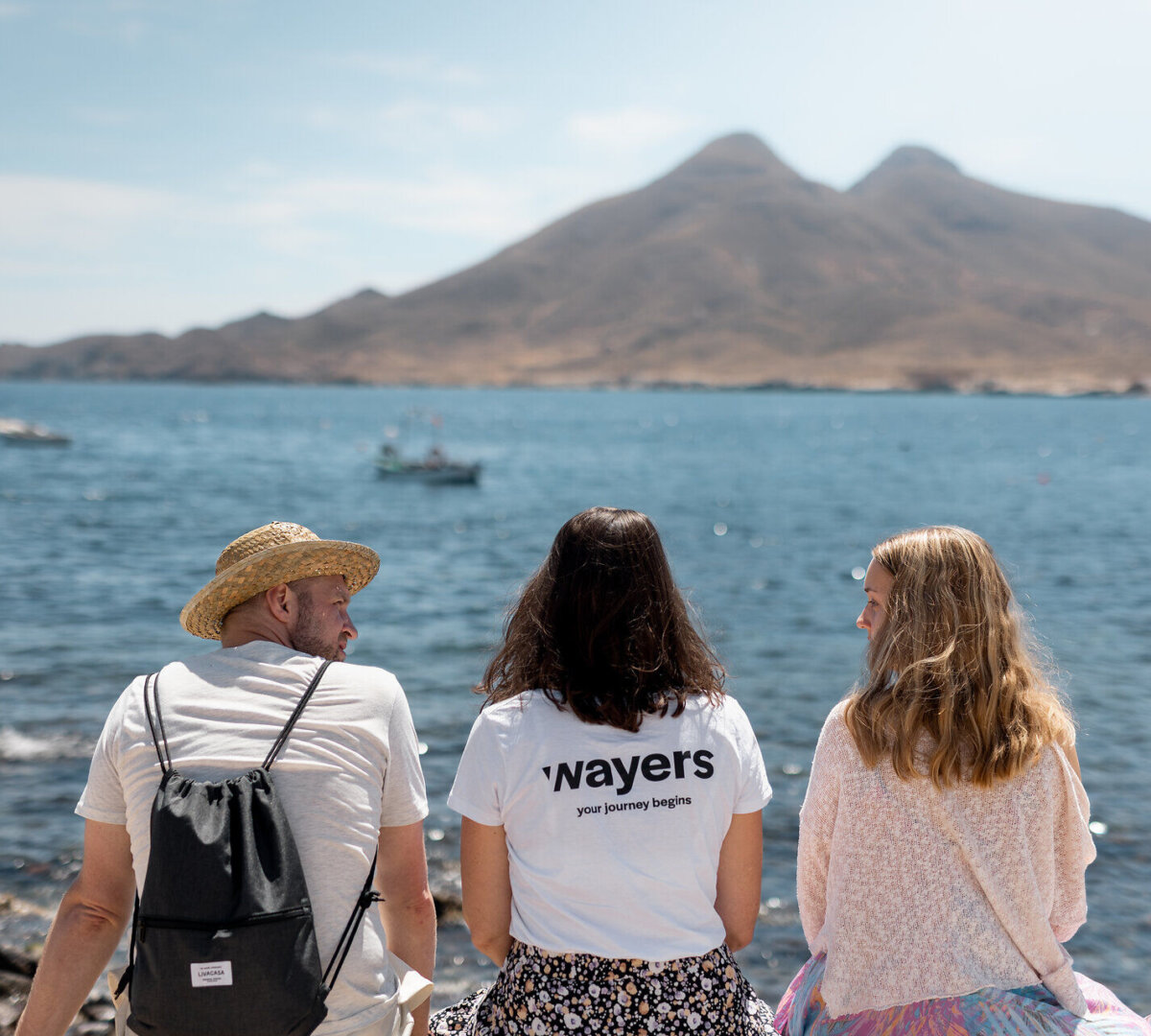 Zwei Frauen und ein Mann sitzen auf Felsen und blicken aufs Meer.