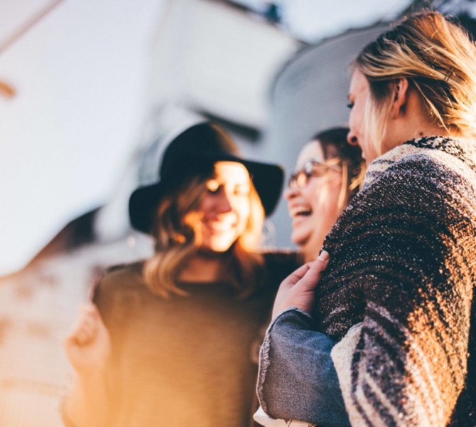 Drei Frauen lachen gemeinsam im Sonnenlicht, in entspannter Atmosphäre im Freien – Moment der Freundschaft und Freude.