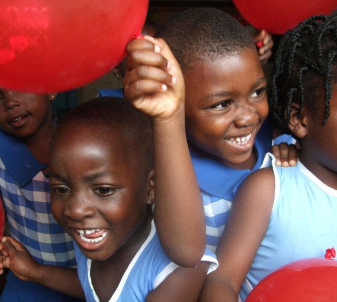 Lachende Kinder mit roten Luftballons in Schuluniform bei fröhlicher Aktivität im Rahmen von Sozialarbeit mit Kindern in Ghana
