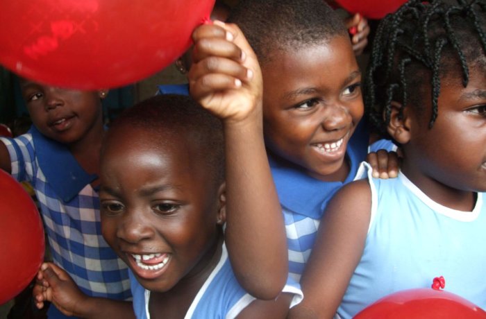 Lachende Kinder mit roten Luftballons in Schuluniform bei fröhlicher Aktivität im Rahmen von Sozialarbeit mit Kindern in Ghana