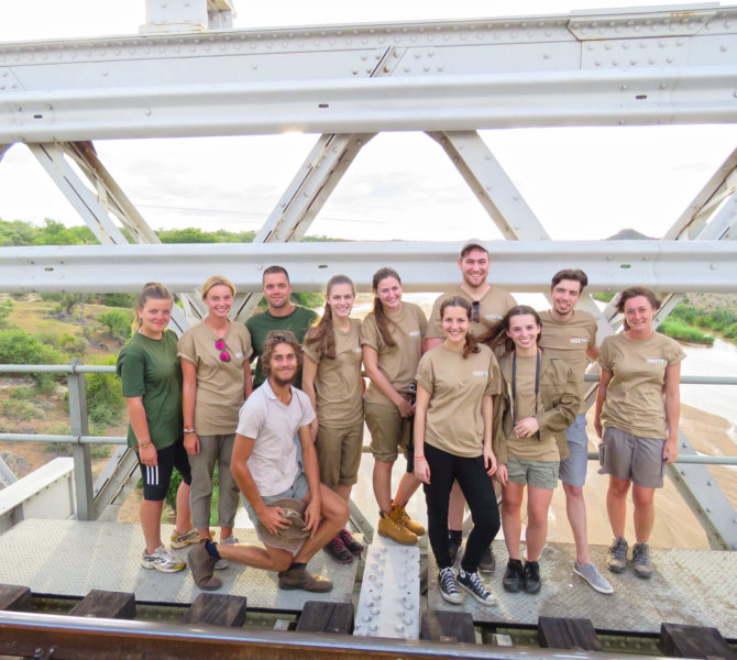 Wayers Gruppe von Freiwilligen posiert auf Eisenbahnbrücke mit Blick auf Fluss und grüne Landschaft im Hintergrund