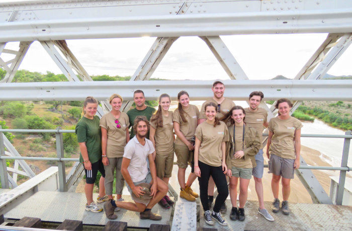 Wayers Gruppe von Freiwilligen posiert auf Eisenbahnbrücke mit Blick auf Fluss und grüne Landschaft im Hintergrund