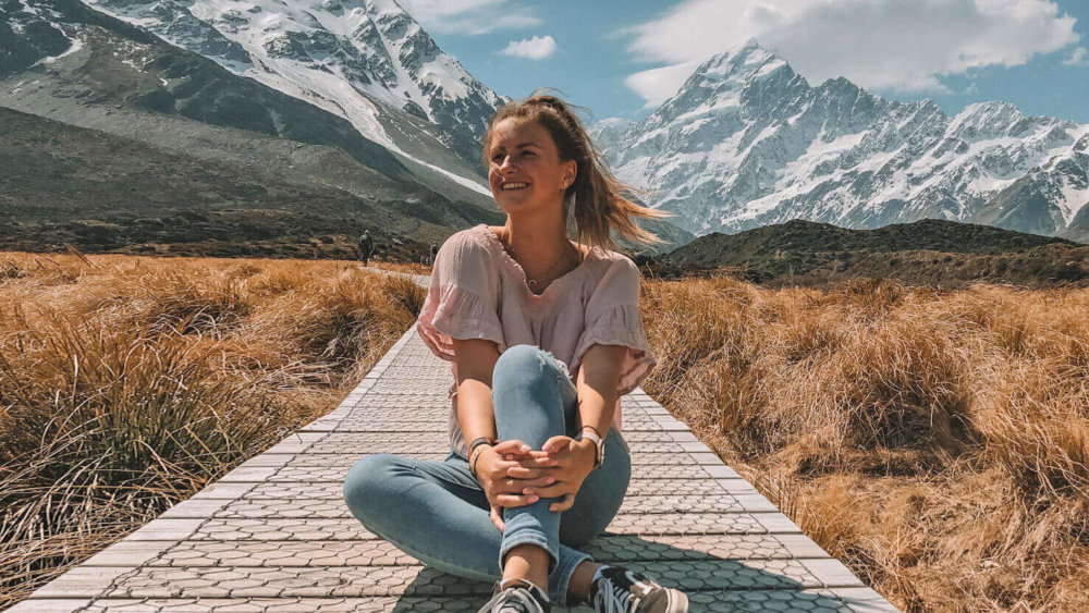 Mädchen sitzt auf einem Steg in mitten einer schönen Landschaft in Neuseeland