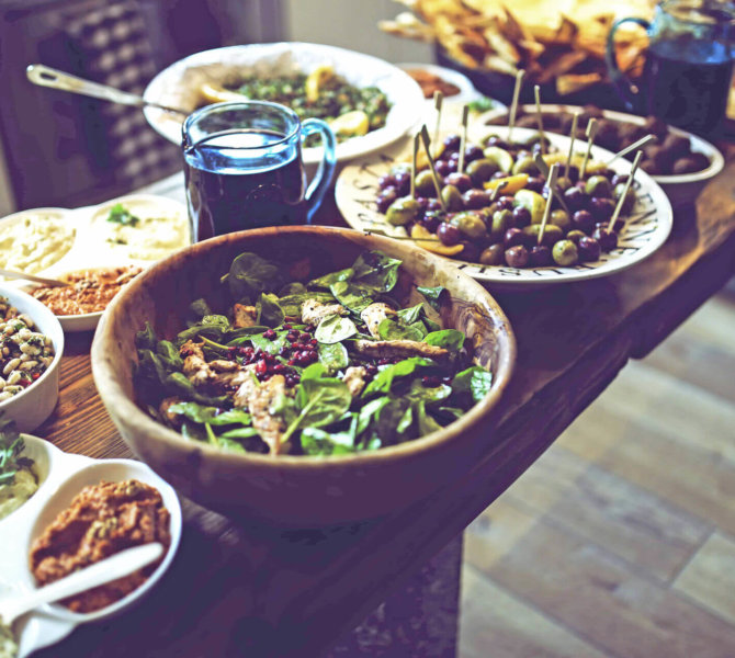 Vielfältiges Buffet mit Salaten Dips Oliven und weiteren Speisen auf einem rustikalen Holztisch in gemütlicher Atmosphäre