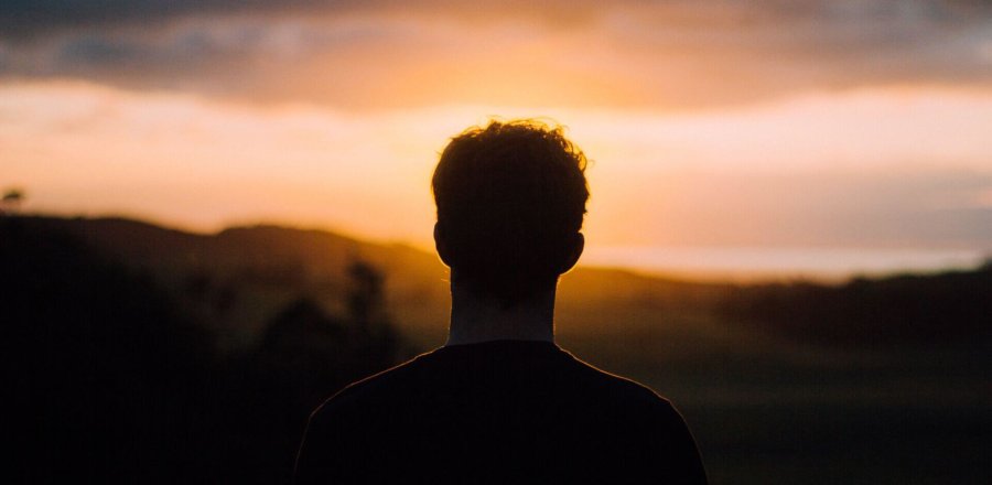 Mann steht vor Sonnenunterganag und blickt in die Ferne