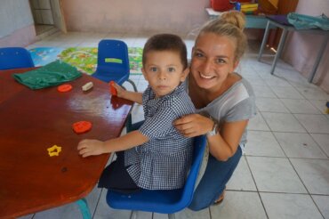 Junge Frau spielt mit Kind am Tisch in bunter Kindertagesstätte bei einem Sozialarbeitsprojekt mit Kindern in Costa Rica.