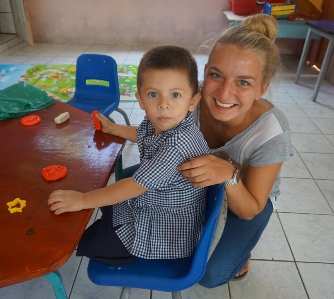 Junge Frau spielt mit Kind am Tisch in bunter Kindertagesstätte bei einem Sozialarbeitsprojekt mit Kindern in Costa Rica.