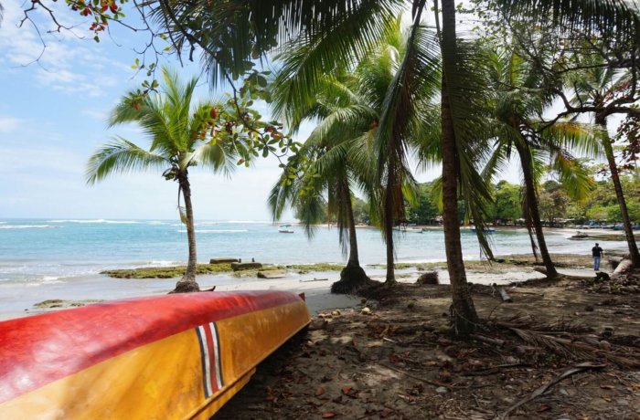 Ein buntes Boot liegt unter Palmen an einem ruhigen Strand mit Blick aufs Meer in Costa Rica.