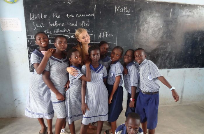 Mädchen stehen mit Teilnehmerin vor einer Schultafel, freiwilligenarbeit, kinder, sozialarbeit-mit-kindern, unterrichten