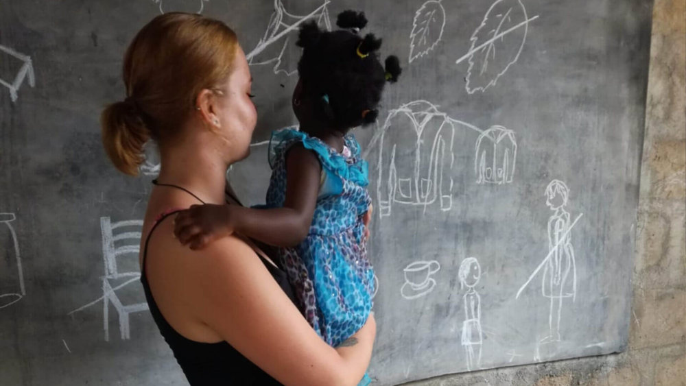 kira-hat-maedchen-auf-dem-arm-und-malt-an-tafel