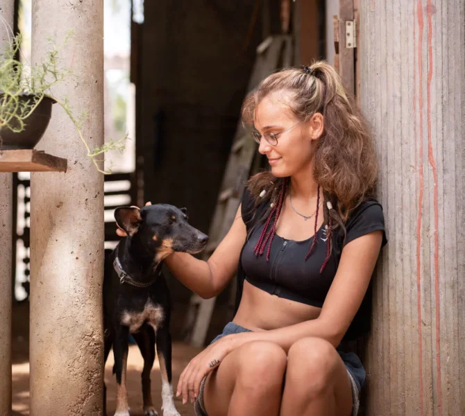 Freiwillige streichelt Hund und sitzt entspannt im Eingang einer Tierstation während Tierschutzprojekt in Mexiko