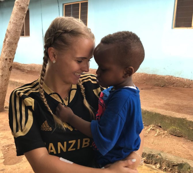 Freiwillige hält Kind im Arm und lächelt liebevoll während Sozialprojekt auf Sansibar