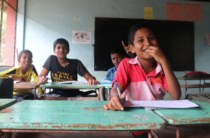 Lachende Kinder sitzen an Schulbänken und schreiben in ihre Hefte während eines Bildungs- und Sozialarbeitsprojekts mit Kindern in Sri Lanka