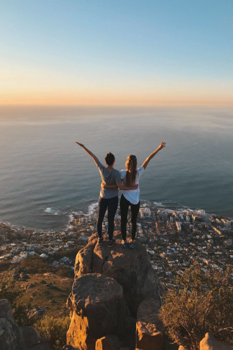 Zwei Personen stehen auf Felsen mit Blick auf Stadt und Meer bei Sonnenuntergang in Südafrika
