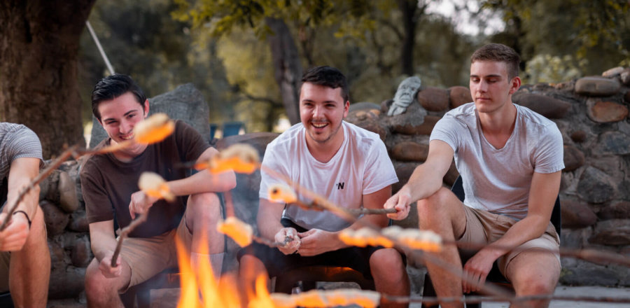 Gruppe junger Männer sitzt entspannt am Lagerfeuer und grillt Brot inmitten der Natur beim Wildlifeprojekt im Krüger Nationalpark in Südafrika